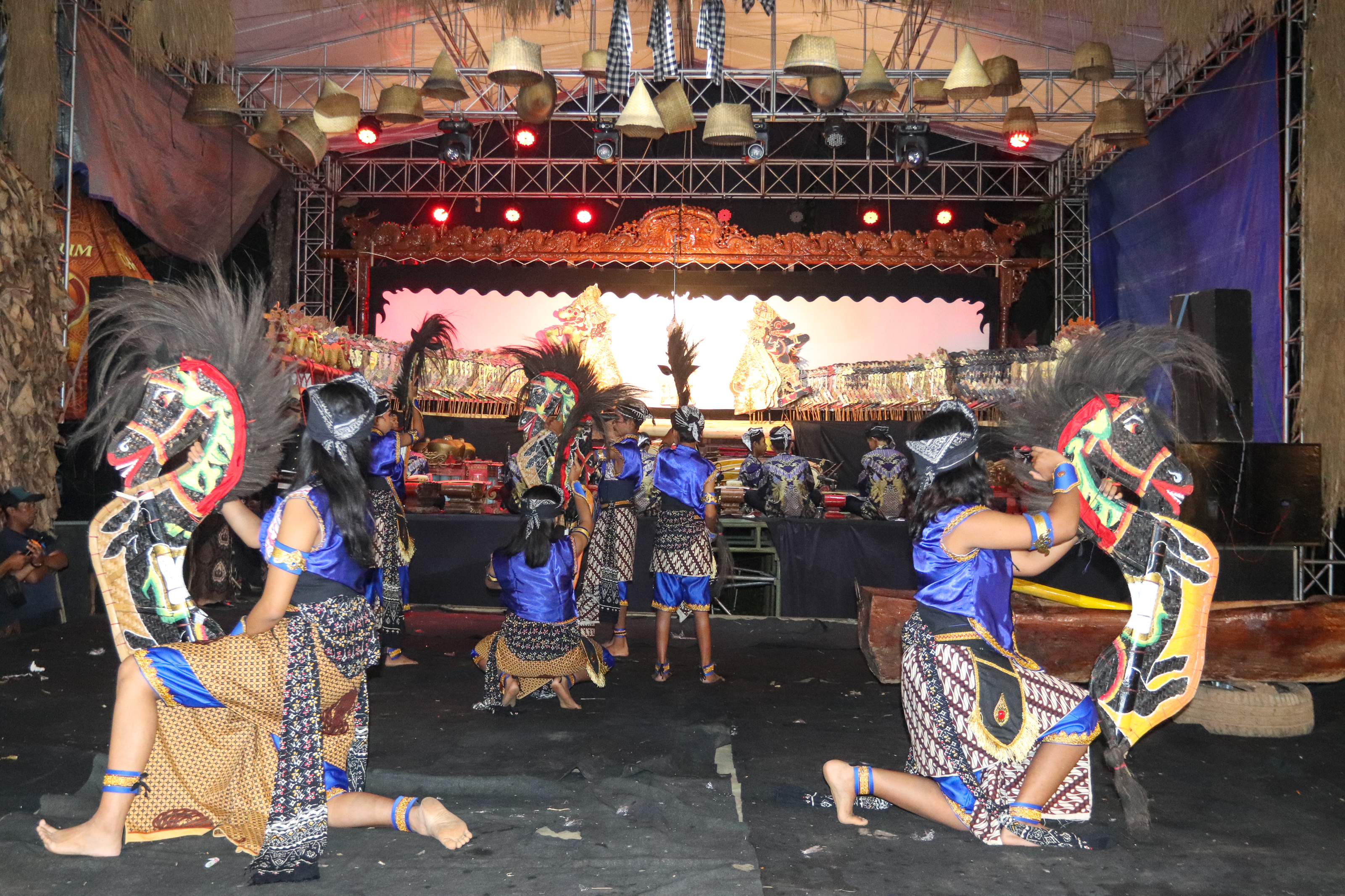 Penari topeng bergaya tradisional Jawa dalam pose dinamis dengan kostum berwarna cerah dan properti tari